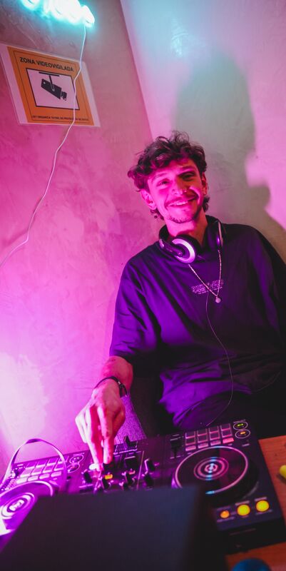 A DJ playing a set on a controller under pink and violet lighting.