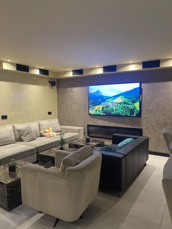 A quiet lounge with a long sofa, a fireplace and a large screen showing a mountain landscape.
